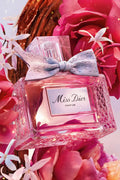 Miss Dior Parfum by Dior surrounded by pink roses and jasmine flowers showcasing its floral and fruity fragrance inspiration.