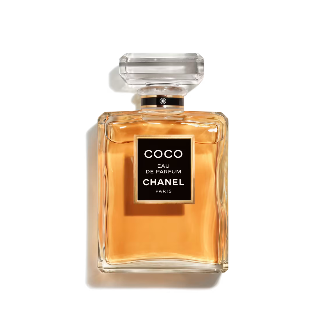 Chanel Coco Eau de Parfum 100ml fragrance bottle featuring a clear glass design, warm amber-colored perfume, black signature label, and transparent faceted cap against a black background.