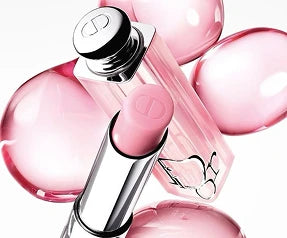 Dior Addict Lip Glow balm tube in a light pink shade with matching aesthetic liquid droplets on ZARÉ Cosmetics.