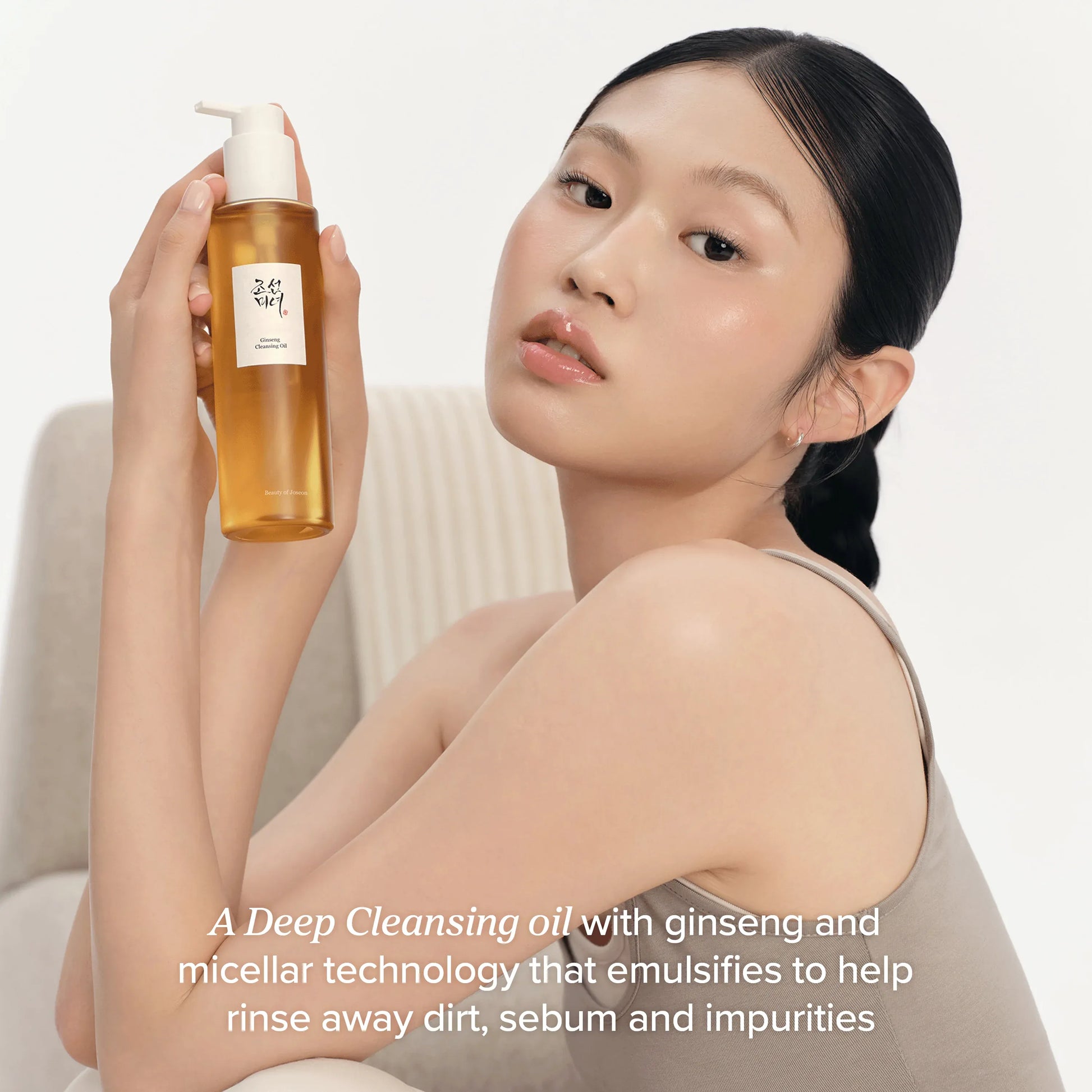 Model holding Beauty of Joseon Ginseng Cleansing Oil bottle showing amber oil texture and pump packaging on clean white background.
