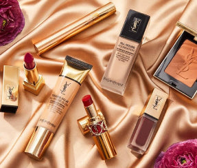 YSL Beauty makeup collection including All Hours foundation, lipsticks, and blush flat lay on silk fabric at ZARÉ Cosmetics